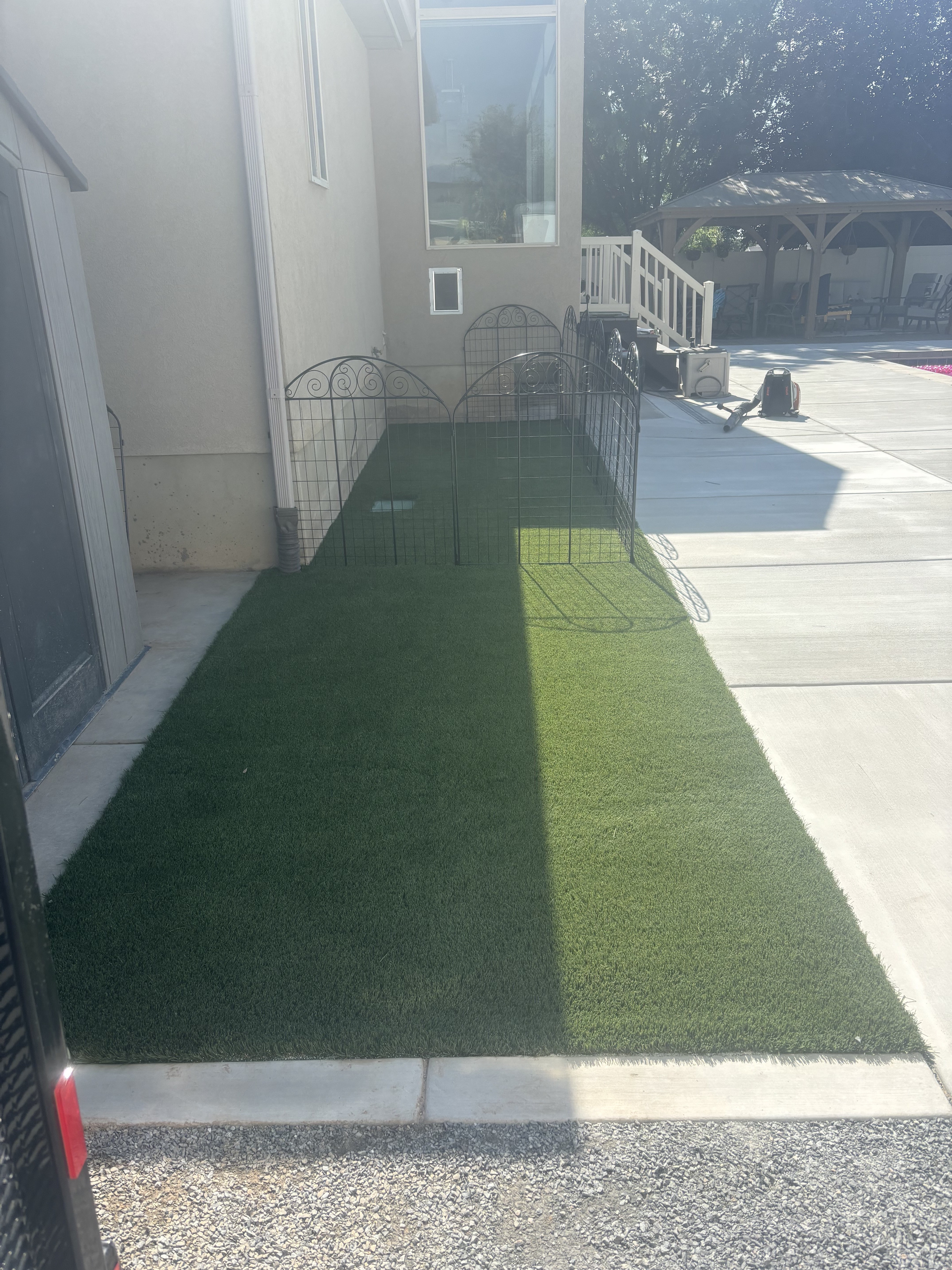 Side yard synthetic turf strip beside concrete driveway with metal garden fencing