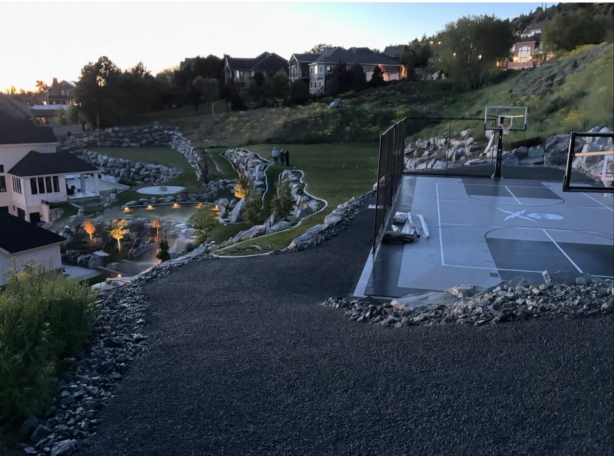 Hillside estate outdoor build with rock waterfall and sport court at sunset