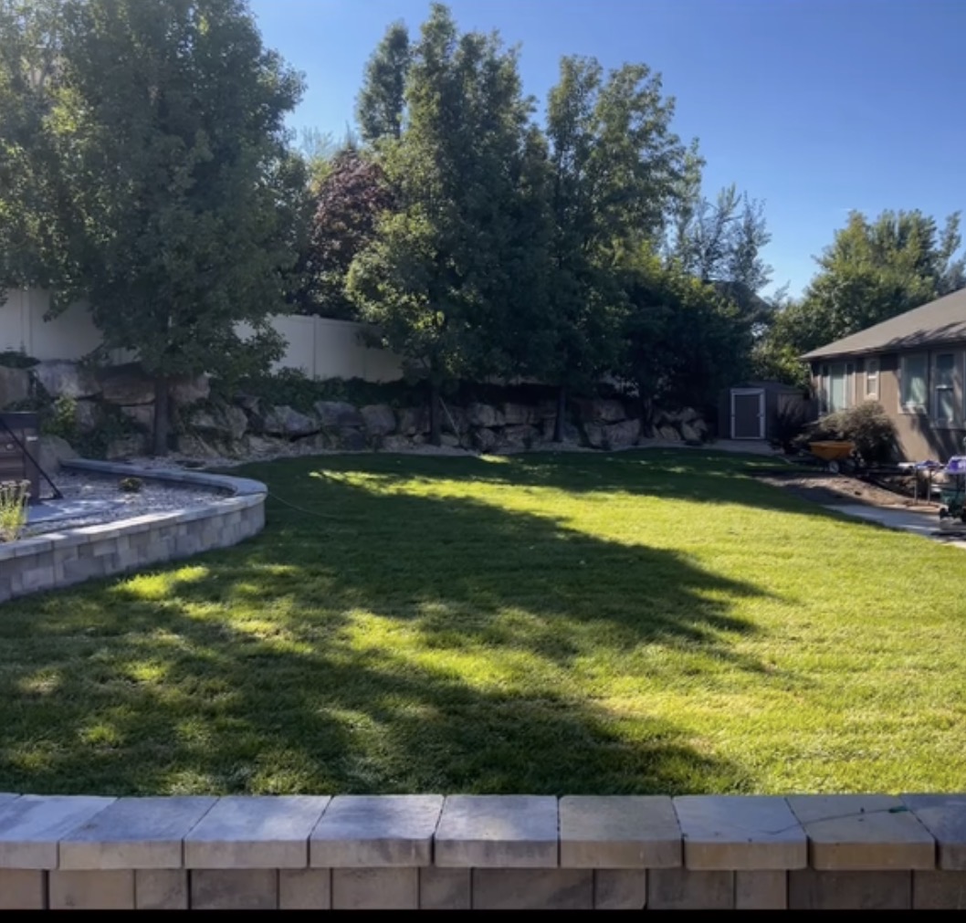 Boulder retaining wall with mature trees and lawn