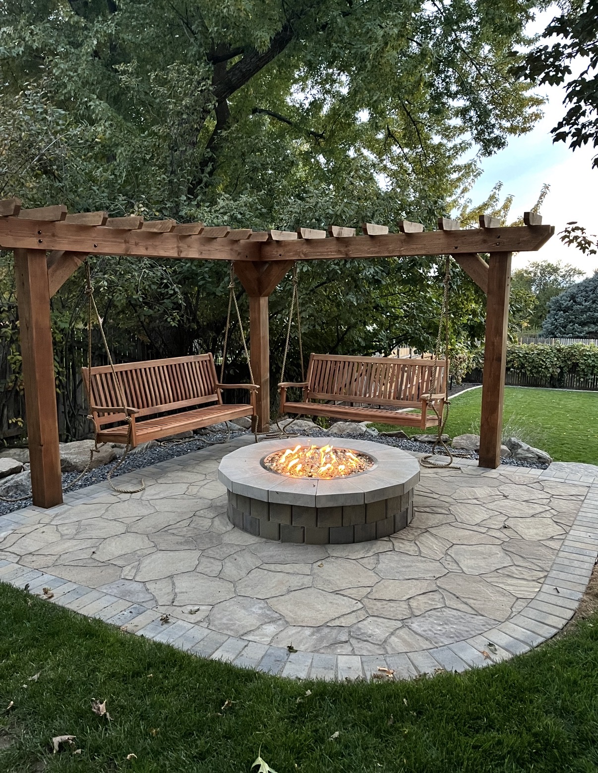Cedar pergola with hanging swings and stacked stone fire pit