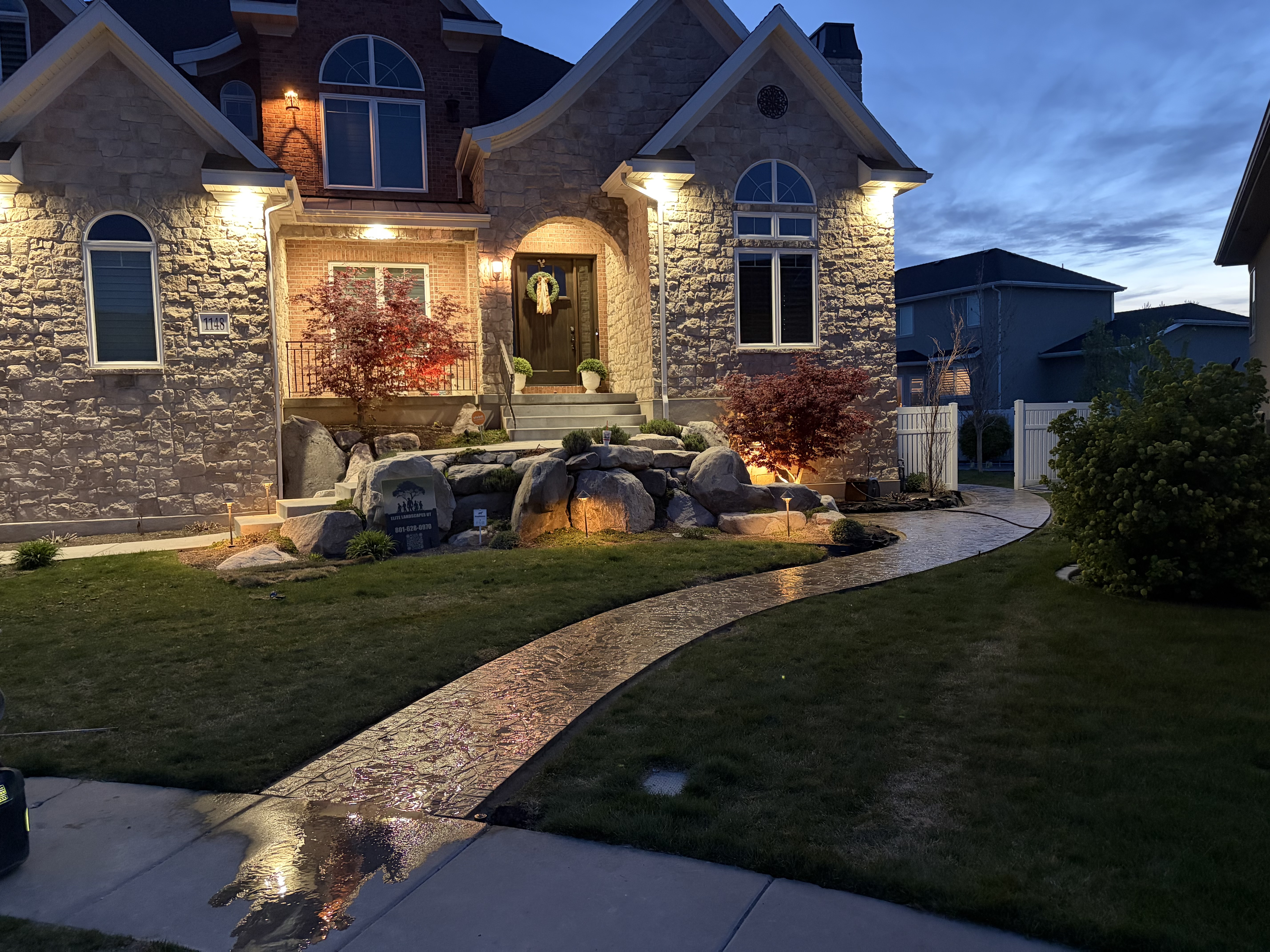 Stamped paver walkway at night with uplighting on stone clad home