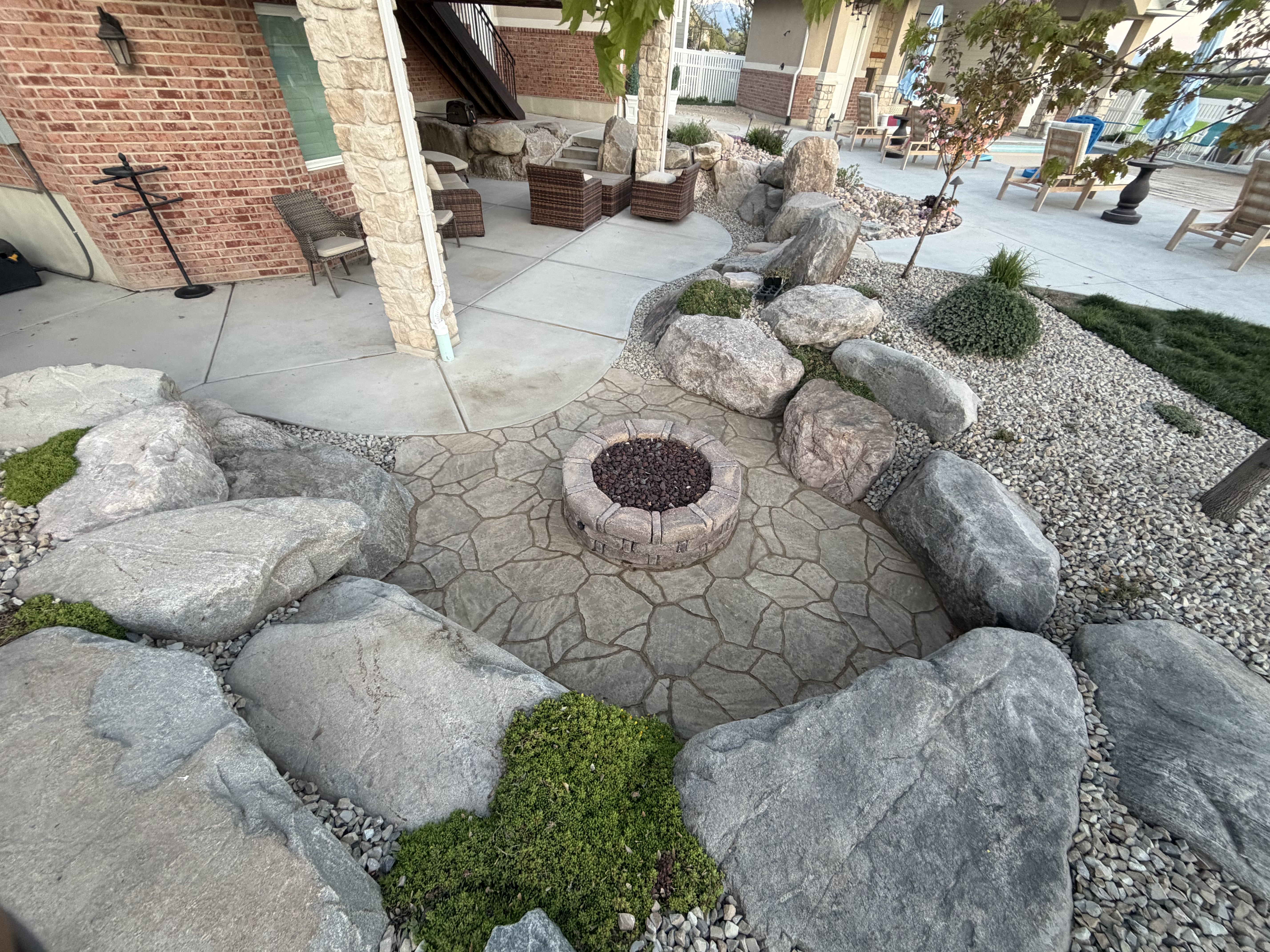 Stacked stone fire pit on stamped patio with boulder surround